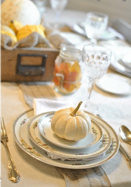 a refined vintage Thanksgiving tablescape with exquisite plates and saucepans with gold patterns, a crate with pumpkins and a leaf covered jar is very beautiful