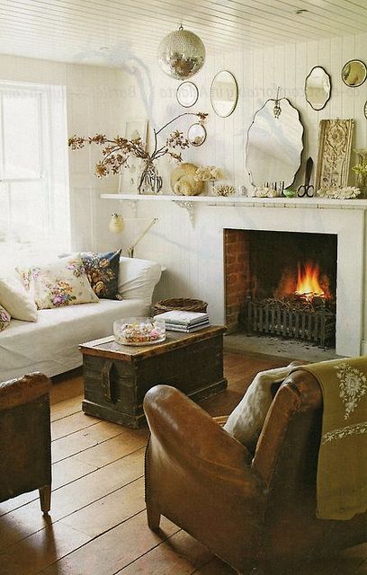 a neutral vintage living room with a white sofa, a fireplace, a brown chair, a chest as a coffee table and an arrangement of mirrors