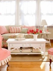 a pretty cottage living room with pink chairs and a floral sofa, some printed pillows, a white coffee table and vintage lamps