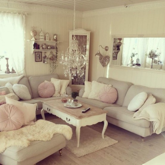 a neutral vintage living room with neutral sofas, a low coffee table, some pillows and blankets, wall-mounted shelves, a mirror and a chic chandelier