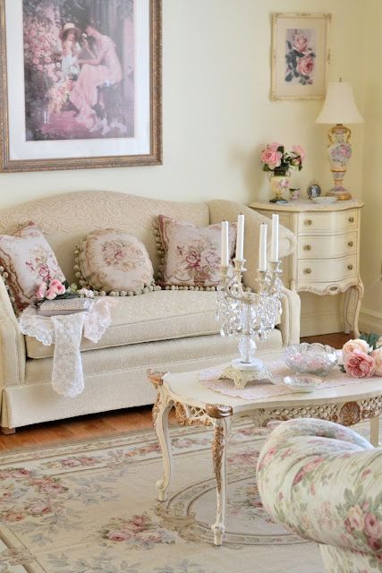 a vintage living room with a tan sofa, a white credenza, a refined coffee table, floral chairs, a floral rug and some floral pillows and artworks
