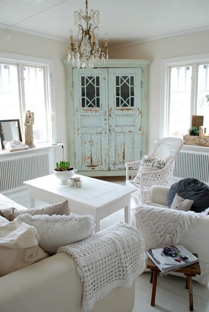 a charming shabby chic living room with neutral sofas, white chairs, a low coffee table and a corner cabinet with mint green doors