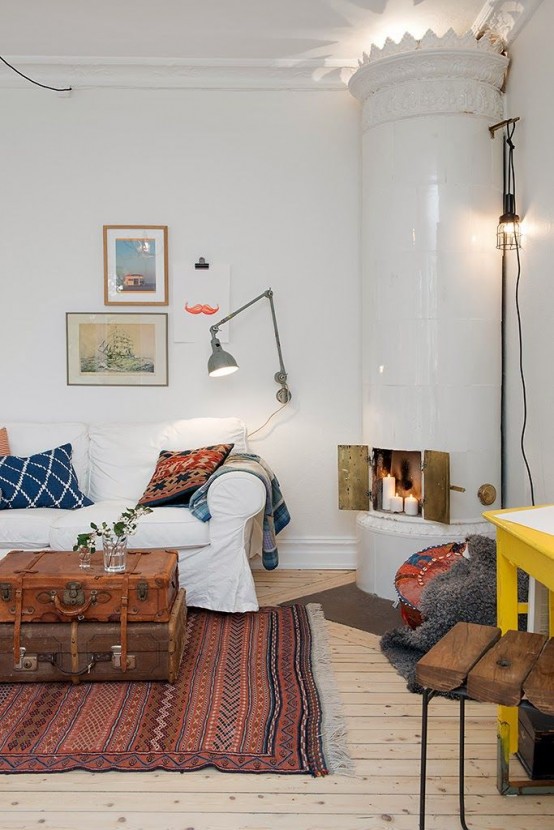 a vintage Scandi living room with a traditional stove, a white sofa with printed pillows, a stained chest, a gallery wall and a printed rug is a cozy space