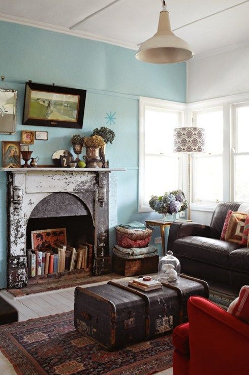 a vintage meets eclectic living room with a blue accent wall, a non-working fireplace used for book storage, a gallery wlal and a pendant lamp plus a chest as a coffee table