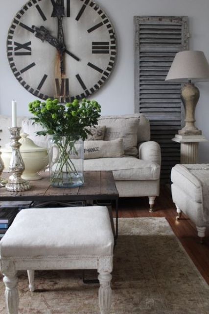 a neutral vintage living room with seating furniture, a coffee table and an ottoman, a large clock and some cool lamps is a lovely space to be in