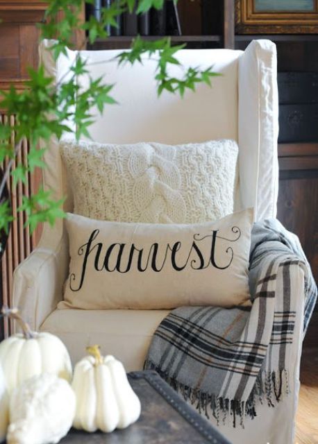 a creamy chair with some fall pillows and a neutral plaid blanket is a cool idea to feel cozy in the fall and at Thanksgiving
