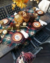 a cozy woodland Thanksgiving tablescape with a plaid table runner, moss, antlers, pinecones, metal chargers and cool plates plus fall leaves