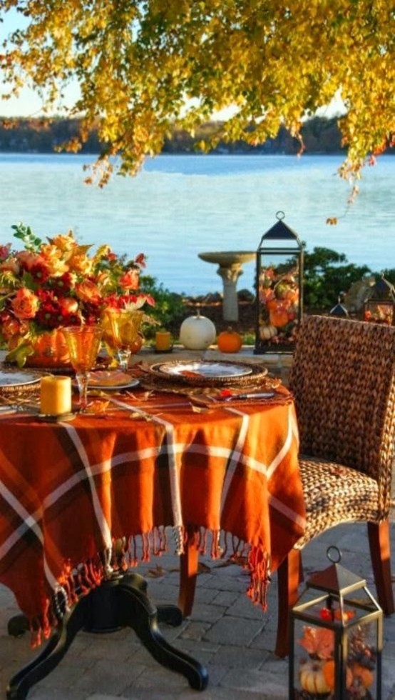 a Thanksgiving tablescape with a bright plaid tablecloth, a bold fall-colored floral centerpiece, amber glasses and a cool view