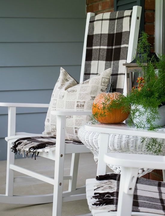 a white rocker with a plaid blanket, printed pillows, a pumpkin and potted greenery is a chic idea for fall and Thanksgiving
