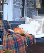 a fall bench with neutral printed fall pillows, a pumpkin and a plaid blanket is a stylish and chic idea to go for