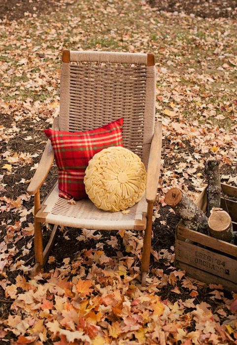 a wicker chair with a duo of pillows - a neutral round pillow and a red plaid pillow is a cool solution for a fall or Thanksgiving porch