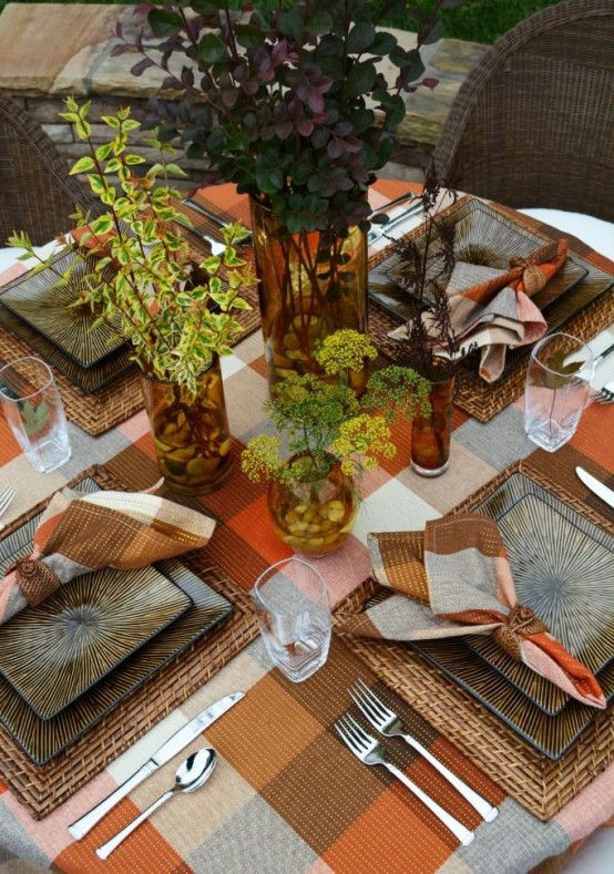 a cozy and lovely Thanksgiving wedding tablescape with a plaid tablecloth, woven chargers and green and grey plates, a cluster centerpiece of greener, branches and blooms is super welcoming