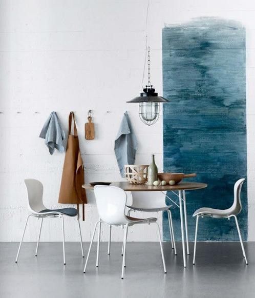 a seaside dining space with a blue watercolor accent wall, a lightweight table and matching chairs, a metal pendant lamp on chain
