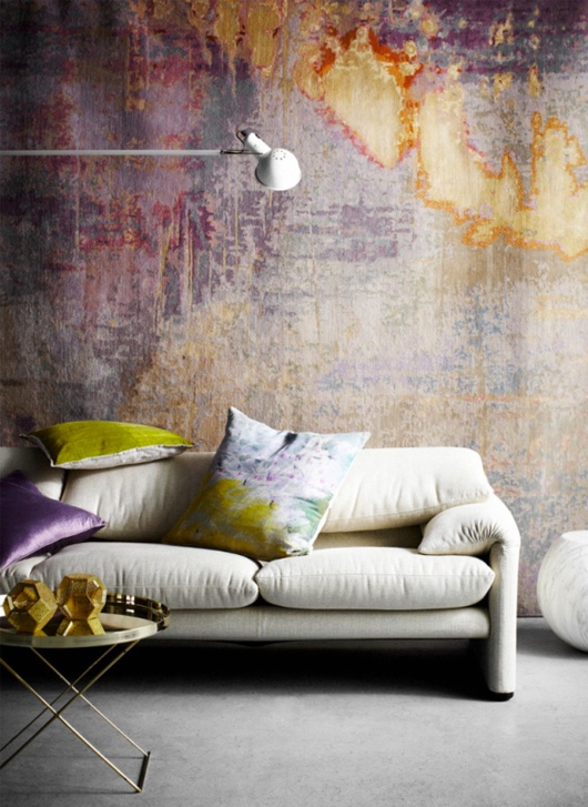 a bright living room with a bold and moody watercolor accent wall, a neutral sofa with colorful pillows that match, a side table and a neutral lamp
