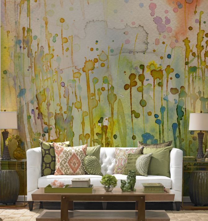a super bright watercolor accent wall with bold splashes of color that imitate blooms, a neutral sofa and colorful pillows, a coffee table with trays and some decor and blooms