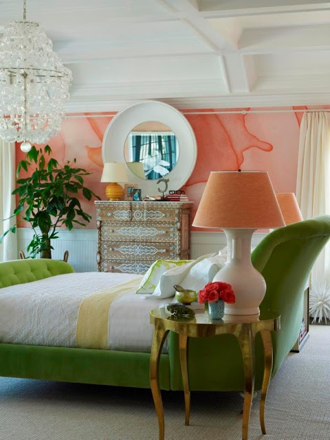 a bright orange watercolor wall, a green upholstered daybed, side tables with orange table lamps and a statement plant