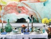 a bright dining space with a colorful watercolor accent wall, a table styled with dishes, bowls, vintage candleholders and bold napkins