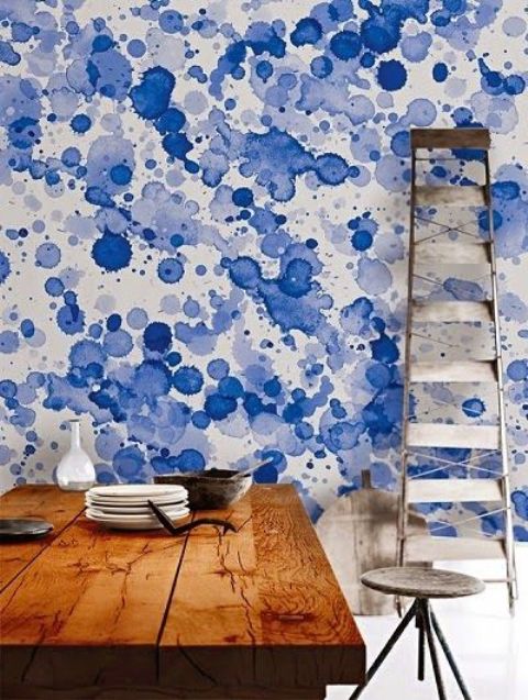 a dining space with a bold blue watercolor wall done with splatters, with a stained table and metal stools, the wall adds color and takes over the space