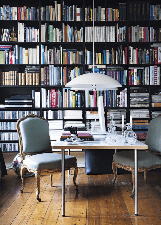 a cozy working space with a bookcase that takes a whole wall, a white desk and light green chairs, white pendant lamps