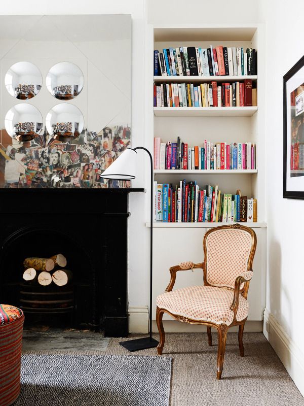 an eclectic living room with a black non working fireplace, built in bookshelves, a series of mirrors and an antique chair redone with polka dot upholstery