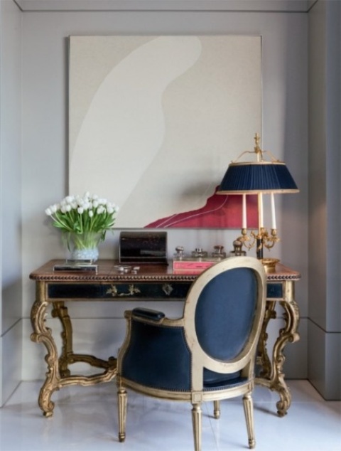 a vintage working nook with a statement print, a vintage black and gold desk, an antique navy and gold chair and a matching table lamp