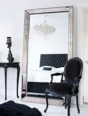 a refined space in white with black furniture for a stark contrast, a black console table, a black antique chair and a large floor mirror in a mirrored frame