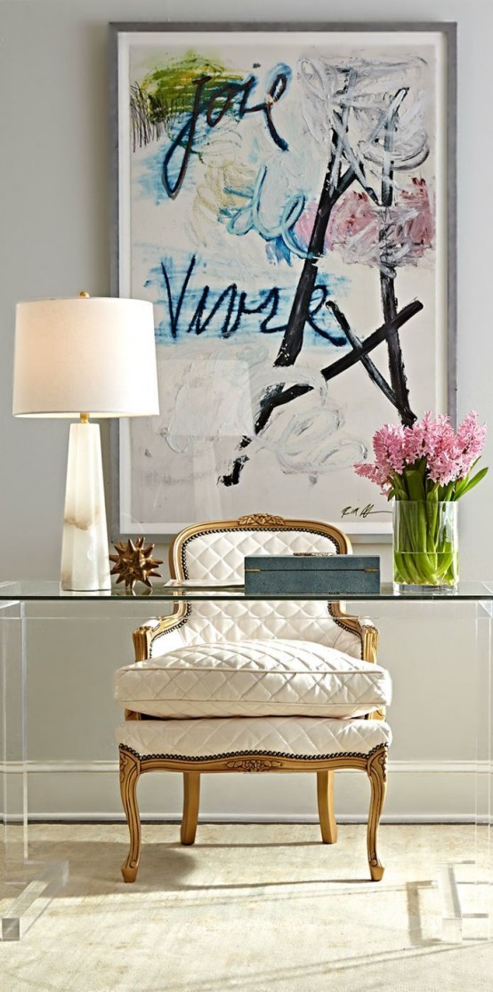 a neutral working space with a bold artwork, a glass desk and an antique white chair with gold touches is a lovely space to spend time in