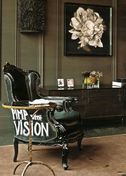 an elegant moody living room with green walls, a glossy black credenza, a green antique chair with a modern touch and an elegant glass side table