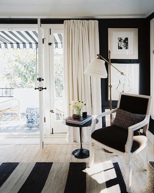 a black and white living room with black walls, a striped rug, an antique black and white chair, white curtains and a side table