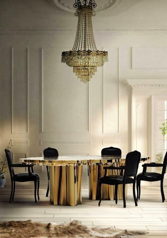 a glam and chic dining space with a fantastic gold and white catchily shaped dining table and antique black chairs, a large crystal chandelier