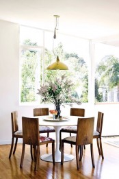 an airy dining room with a round table, antique chairs with floral upholstery and a yellow pendant lamp is a lovely and cozy space