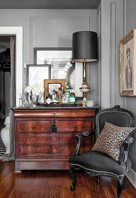 an antique nook with a stained dresser, some artwork and mirrors, a black antique chair, a black table lamp and a leopard print pillow