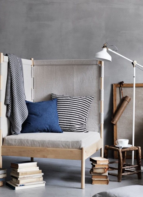 a small reading nook with a chic upholstered chair, pillows, stacks of books and an IKEA Ranarp lamp for light and coziness