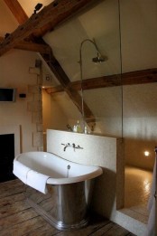 a modern farmhouse bathroom with neutral walls, a ceiling with wooden beams, a metal tub and modern fixtures