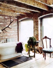 a vintage industrial bathroom with brick walls, wooden beams, a tub, vintage chairs and a striped rug