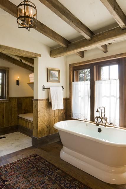 a rustic vintage bathroom with wooden beams, wood paneling on the walls, a boho rug and a tub