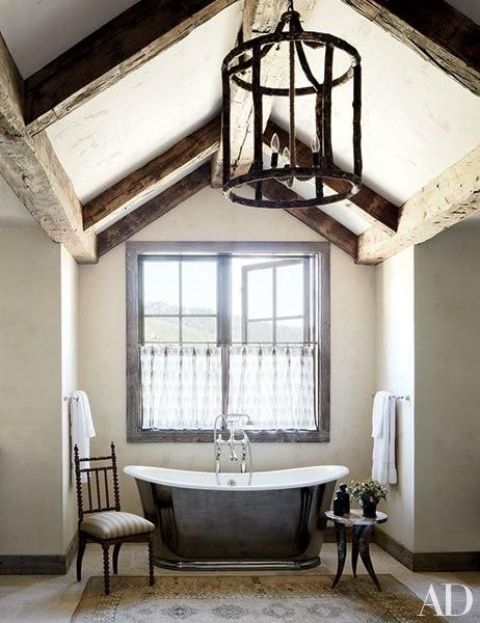 a vintage bathroom with dark wooden beams, a metal clad tub, refined chairs and a vintage chandelier