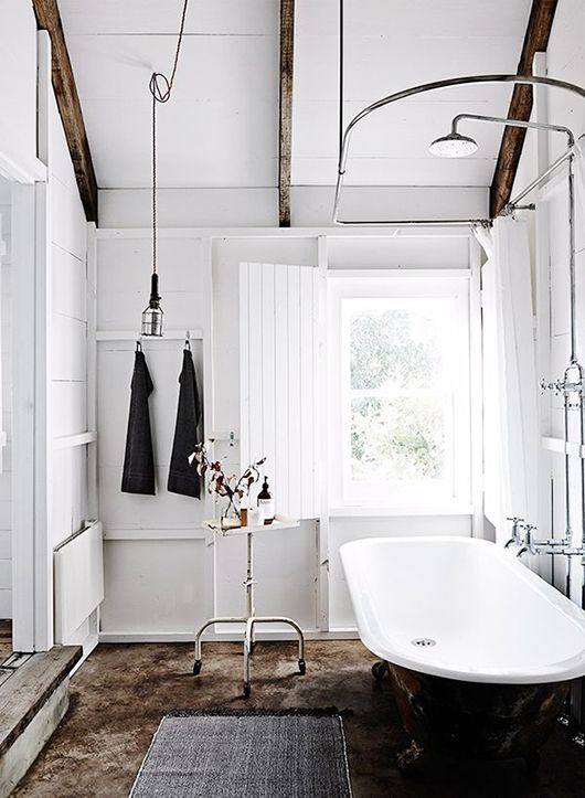 a Scandinavian bathroom with white walls, wooden beams, a black tub and metal fixtures