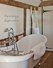 a refined vintage-inspired bathroom in white, with a wooden floor, wooden beams and a chic tub plus vintage fixtures