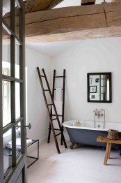 a vintage rustic bathroom with white walls, a grey tub, wooden beams and ladders plus a simple mirror in a wooden frame