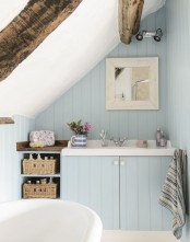 a blue bathroom with light blue walls, wooden beams, a tub and a vanity with a sink