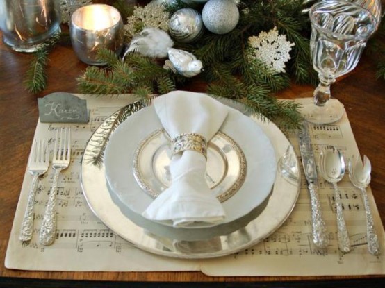 shiny Christmas table decor with a shiny charger and cutlery, white and gold edge plate, evergreens with silver ornaments, candleholders and snowflakes