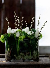 a clear glass vase with greenery, moss, white blooms and willow is a bright and catchy piece for every spring home