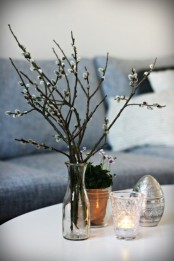 a clear glass vase with willow, some blooms in a pot and a large silver egg for natural and simple spring decor