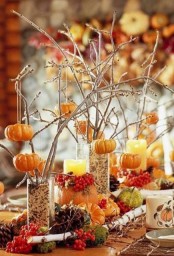 cute fall centerpiece of branches put into glasses with some filler and pumpkins hanging on them