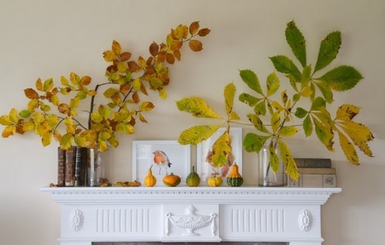 a cool fall mantel with fake fruits and pumpkins and branch and leaf arrangements for a touch of color