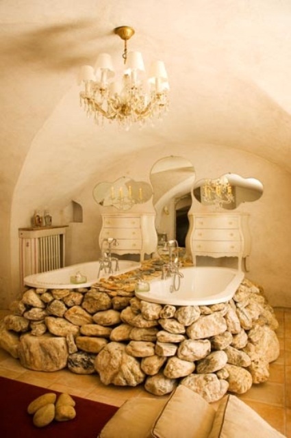 a unique cave-like bathroom with a crystal chandelier, vintage dressers and a couple of bathtubs clad with real stones