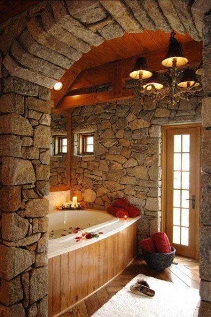 a cabin bathroom with walls all clad with natural stone and a bathtub clad with wood for a cozy feeling