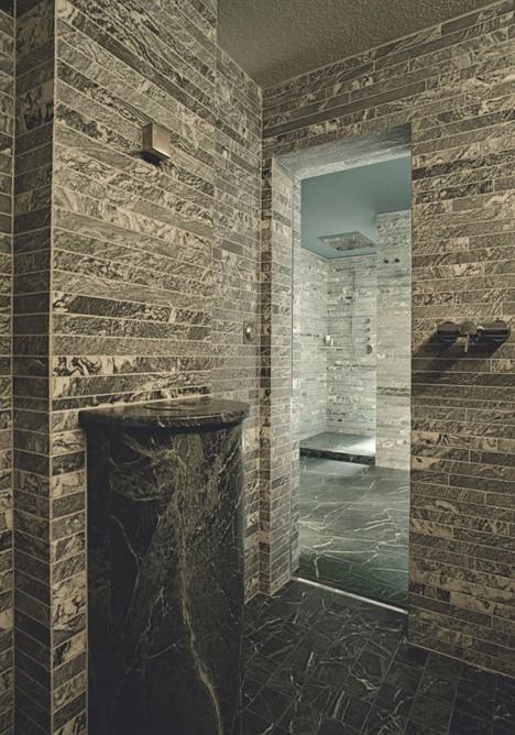 a minimalist bathroom fully clad with tiles that imitate real stone and a stone fre-standing sink