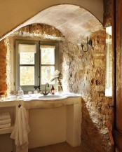 walls of real rough stone are highlighted with an arched stone ceiling and a neutral vanity built-in